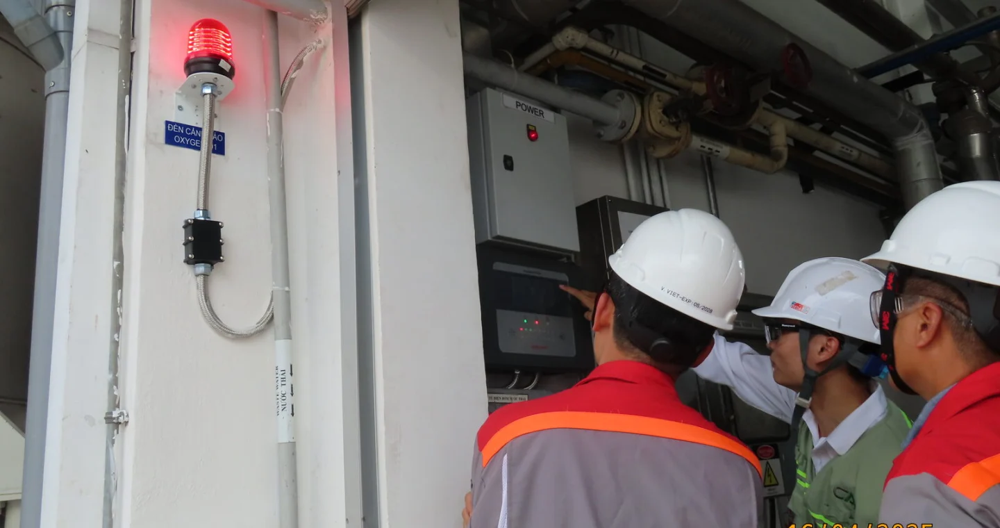 Engineers checking a gas detection panel and warning beacon at a plant
